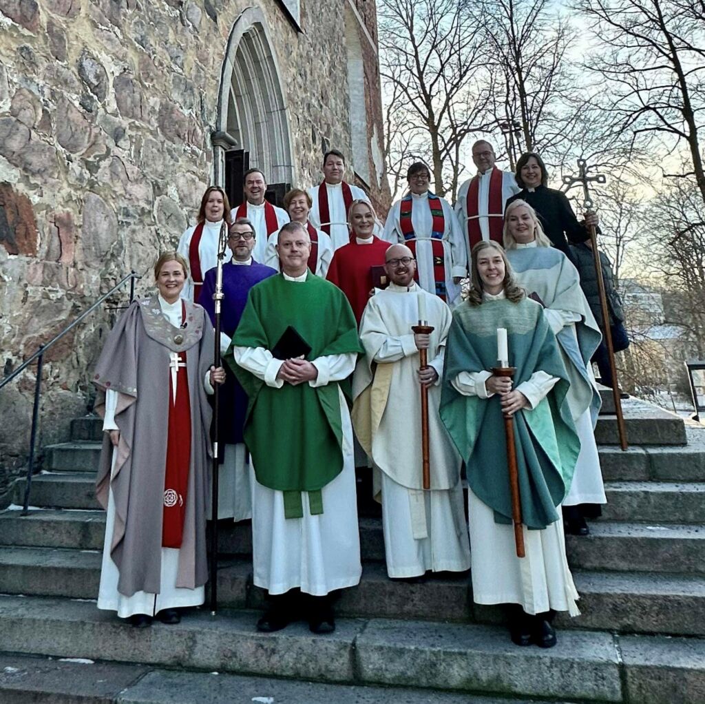 Ihmisiä papin vaatteissa seisoo kivisen kirkon edessä portailla